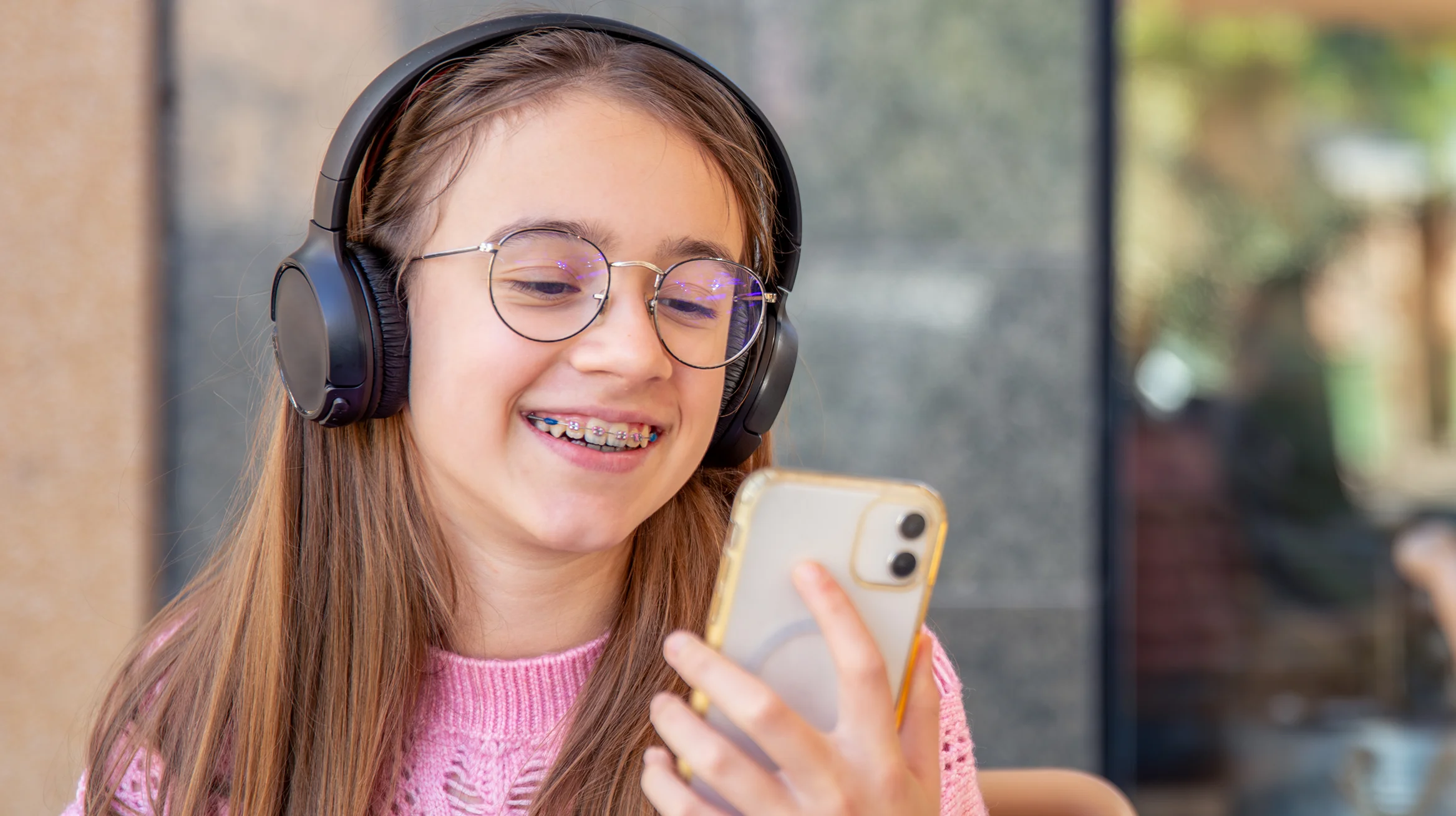 Mädchen mit Zahnspange sitzt entspannt mit Smartphone und Kopfhörern – Alltag mit Zahnspange bei Kindern und Jugendlichen.