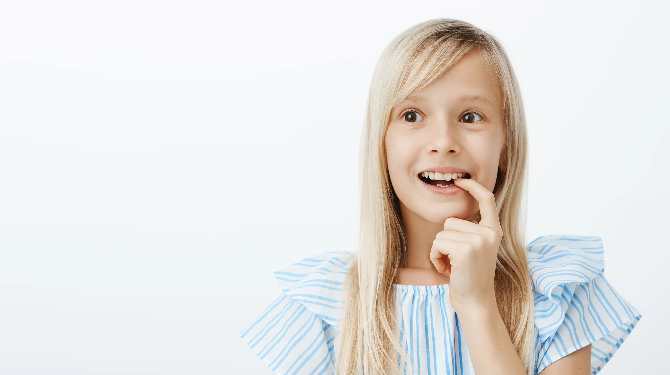 Mädchen zeigt auf ihre Zähne – welche Zahnspange für Kinder geeignet ist.